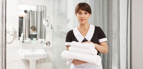i-assure-you-will-have-great-time-our-hotel-portrait-pleasant-caucasian-woman-working-as-housemaid-holding-towels-while-standing-near-bathroom-staring-i-put-them-near-shower-min